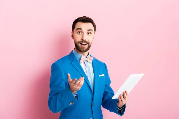 Cheerful bearded businessman holding digital tablet and gesturing on pink — Stock Photo