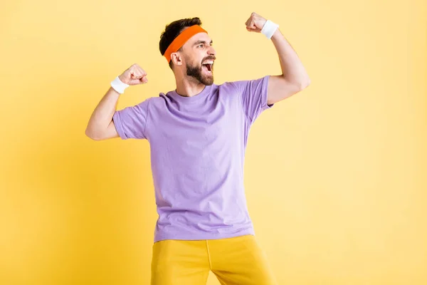 Возбужденный бородатый мужчина показывает мышцы изолированы на желтый — стоковое фото