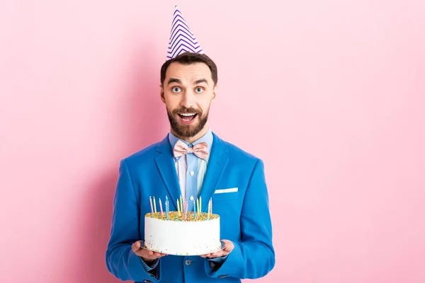 Homem de negócios alegre que mantém o bolo de aniversário com velas no rosa — Fotografia de Stock