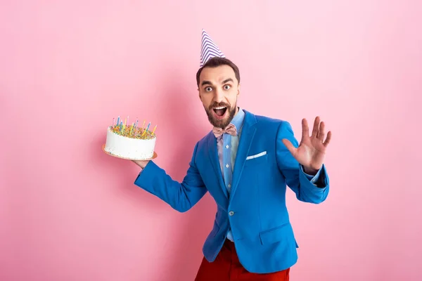 Excited businessman holding birthday cake and looking at camera on pink — Stock Photo