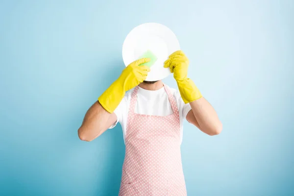 Man holding sponge near plate and covering face on blue — Stock Photo
