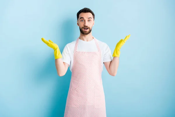 Bearded man in pink dotted apron showing shrug gesture on blue — Stock Photo