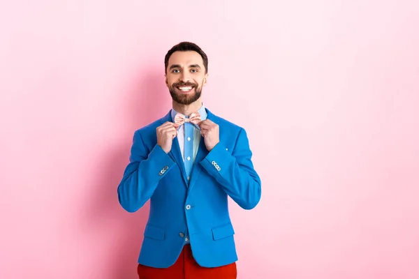 Hombre barbudo feliz en traje tocando pajarita en rosa - foto de stock