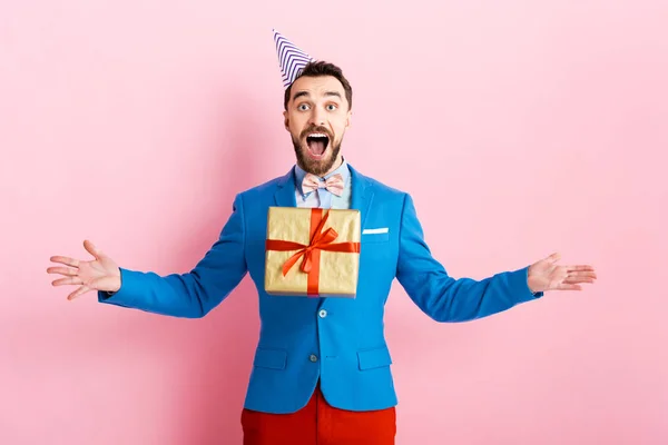 Happy businessman in party cap throwing in air present on pink — Stock Photo