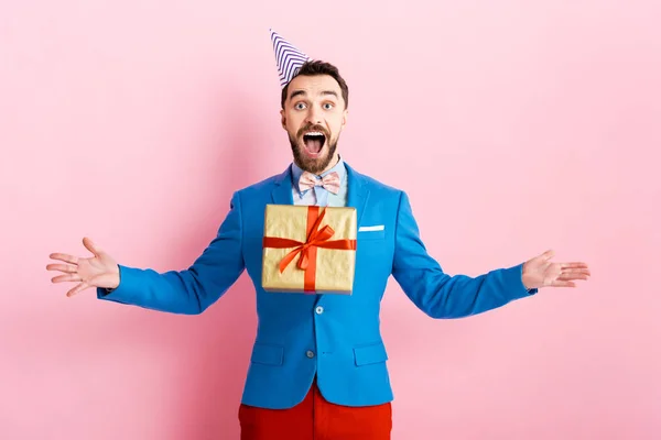 Happy businessman in party cap throwing in air present on pink — Stock Photo