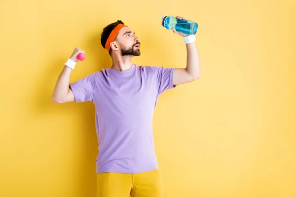 Вид збоку бородатий чоловік тримає спортивну пляшку під час роботи з маленьким гантелі на жовтому — стокове фото