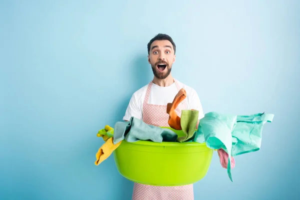 Homme surpris tenant bol de lavage en plastique avec buanderie sale sur bleu — Photo de stock