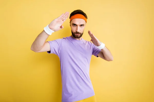 Bearded sportsman in headband working out on yellow — Stock Photo