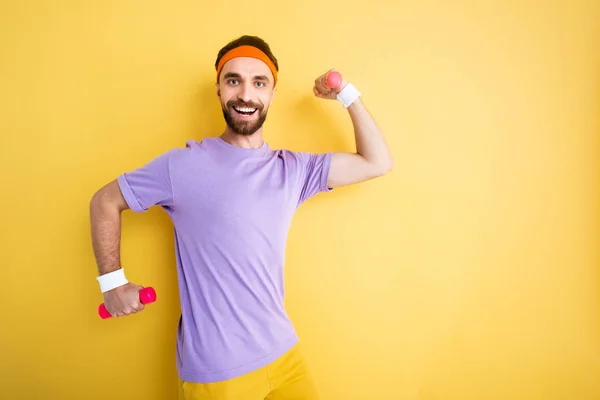 Alegre barbudo deportista sosteniendo pequeñas mancuernas mientras se ejercita en amarillo - foto de stock