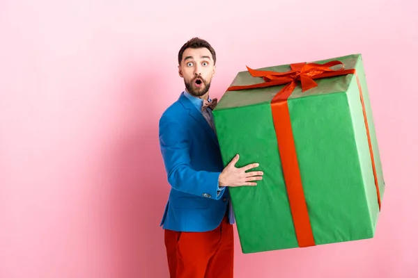 Uomo barbuto sorpreso in possesso di enorme scatola regalo su rosa — Foto stock