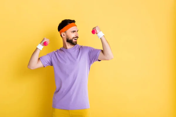 Happy bearded sportsman holding small dumbbells while working out on yellow — Stock Photo