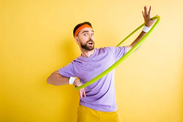 Confused sportsman exercising with hula hoop on yellow — Stock Photo