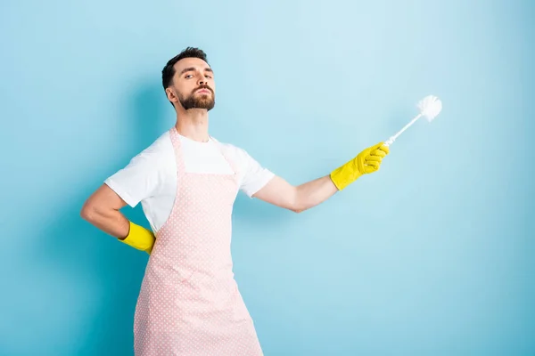 Homme fier dans tablier tenant brosse de toilette sur bleu — Photo de stock