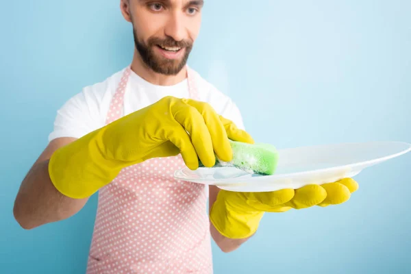 Селективный фокус счастливого бородатого мужчины мыть тарелку с губкой изолированы на синий — стоковое фото