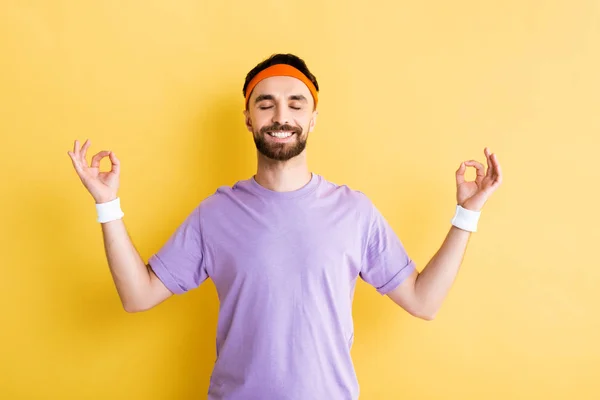 Cheerful man practicing meditation and smiling on yellow — Stock Photo