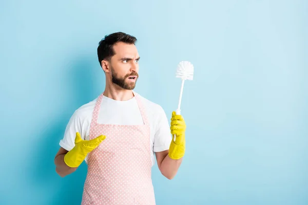 Hombre barbudo disgustado apuntando con la mano al cepillo de inodoro en azul - foto de stock