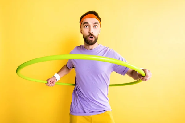 Esportista surpreso exercitando com hula hoop isolado no amarelo — Fotografia de Stock