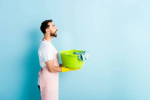 Side view of happy bearded man holding dirty laundry on blue — Stock Photo