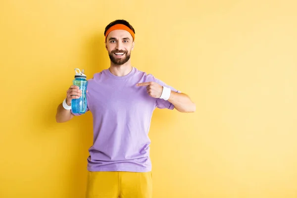 Sportif barbu pointant du doigt la bouteille de sport sur jaune — Photo de stock