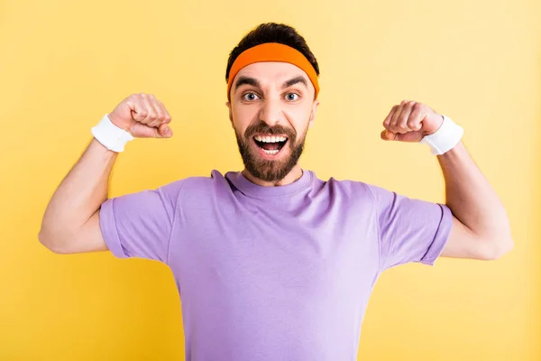 Cheerful bearded sportsman showing muscles isolated on yellow — Stock Photo