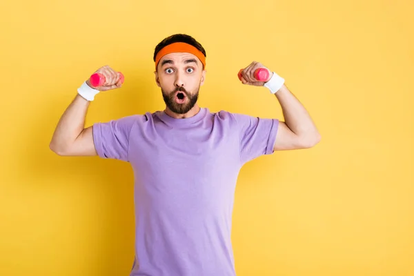 Überraschter Sportler mit kleinen rosa Hanteln auf gelb — Stockfoto