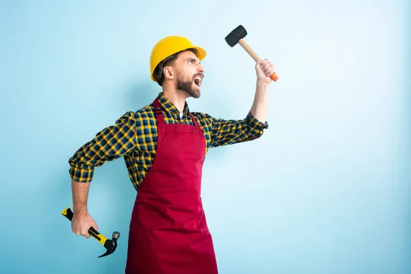 Side view of angry workman holding hammers on blue — Stock Photo