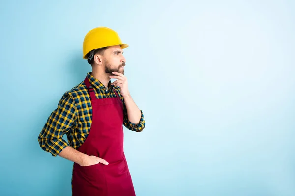 Seitenansicht des nachdenklichen Arbeiters, der mit der Hand in der Tasche auf blau steht — Stockfoto