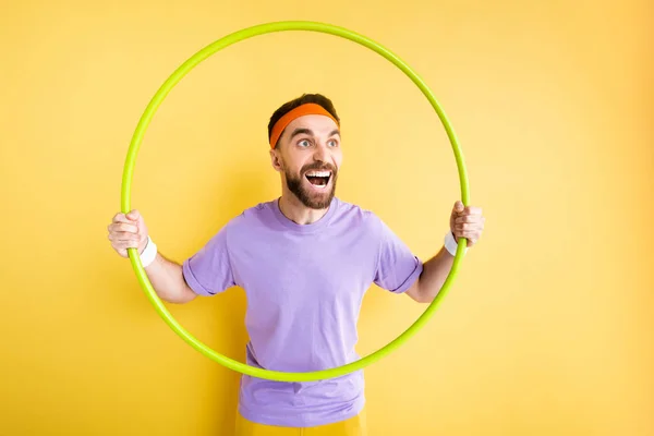 Animado desportista segurando hula hoop no amarelo — Fotografia de Stock