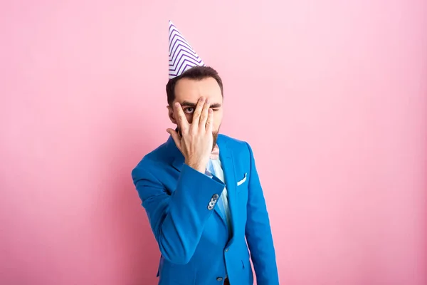 Businessman in party cap covering face on pink — Stock Photo