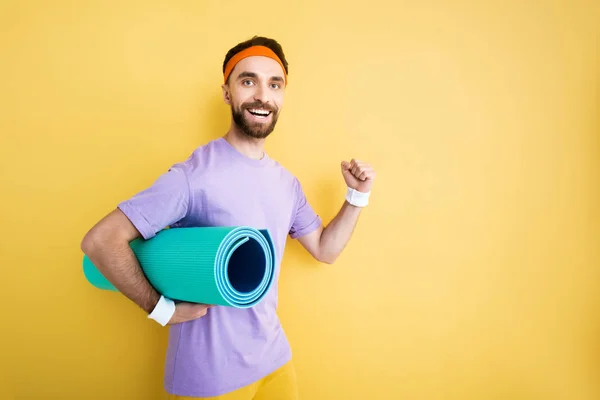 Веселий бородатий спортсмен тримає фітнес килимок на жовтому — стокове фото