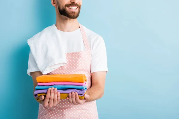 Vista cortada de homem barbudo alegre segurando roupas limpas em azul — Fotografia de Stock