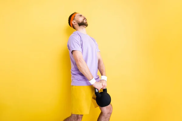 Desportista cansado segurando halteres pesados no amarelo — Fotografia de Stock