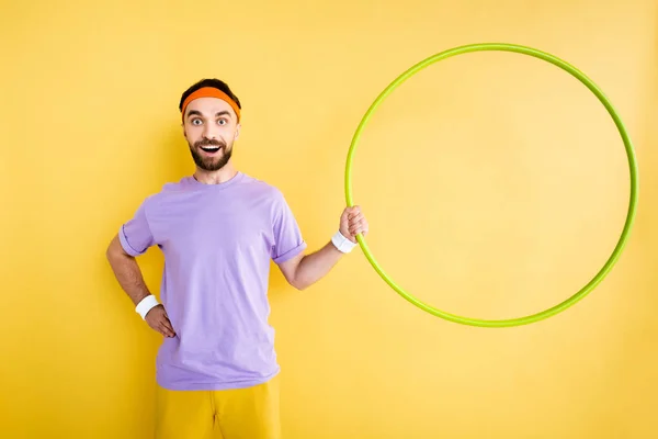 Desportista alegre de pé com a mão no quadril e segurando hula aro isolado no amarelo — Fotografia de Stock