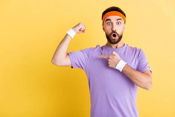 Shocked man in headband pointing with finger and muscle isolated on yellow — Stock Photo