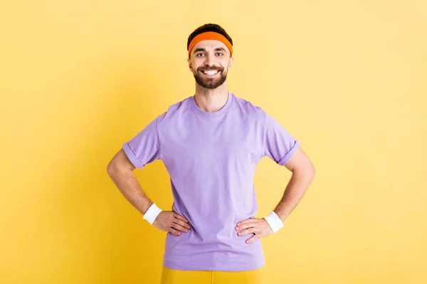 Sportivo felice in piedi con le mani sui fianchi su giallo — Foto stock