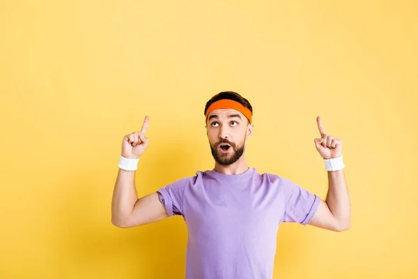 Überraschter Mann mit Stirnband zeigt mit Fingern auf gelb — Stockfoto