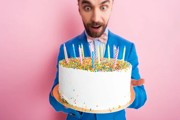 Selective focus candles on tasty birthday cake in hands of man in suit on pink — Stock Photo