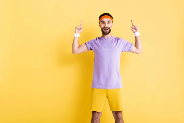 Glücklicher Mann mit Stirnband zeigt mit den Fingern auf gelb — Stockfoto