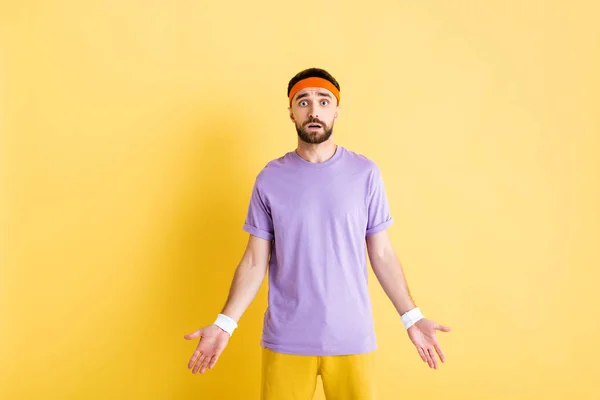 Confused man in headband showing shrug gesture on yellow — Stock Photo