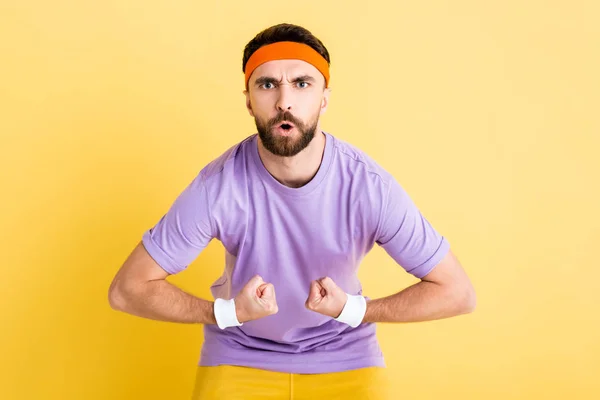 Bearded sportsman in headband showing muscles isolated on yellow — Stock Photo