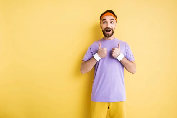 Happy bearded sportsman showing thumbs up on yellow — Stock Photo