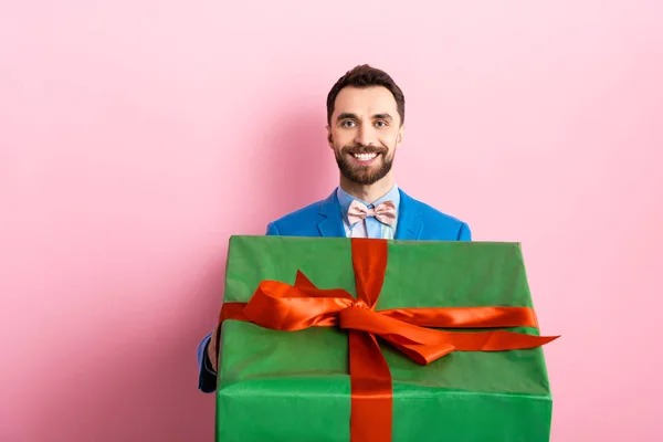 Happy bearded man holding big gift box on pink — Stock Photo