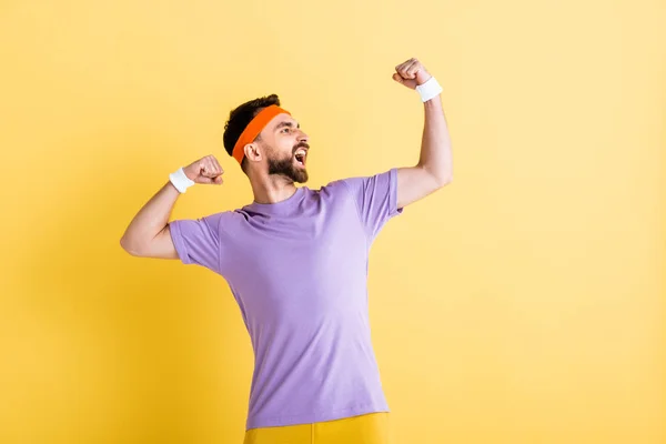 Happy winner in headband screaming while celebrating on yellow — Stock Photo