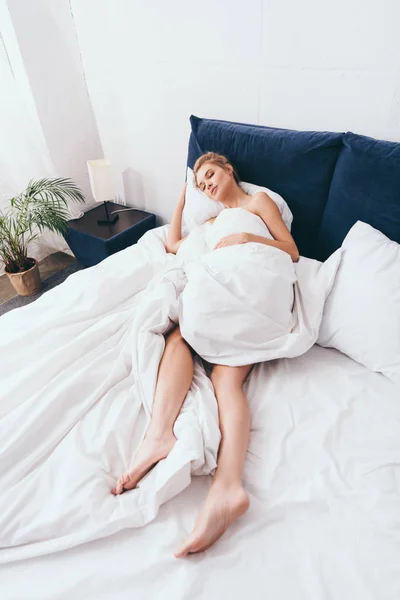 Atractiva mujer durmiendo en sábanas en la cama por la mañana - foto de stock