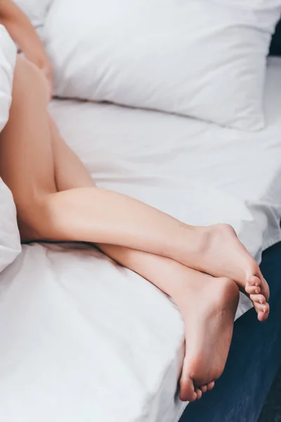 Обрезанный вид женщины лежащей на кровати с белыми простынями — стоковое фото