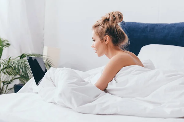 Hermosa mujer usando el ordenador portátil en la cama con sábanas en la mañana - foto de stock