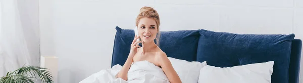 Plan panoramique de femme attrayante parlant sur smartphone dans un lit blanc le matin — Photo de stock