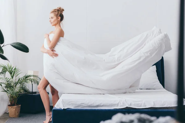 Hermosa mujer sonriente con sábanas blancas en el dormitorio - foto de stock