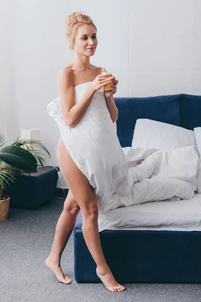 Mulher nua atraente com vidro de suco em folhas brancas no quarto de manhã — Fotografia de Stock