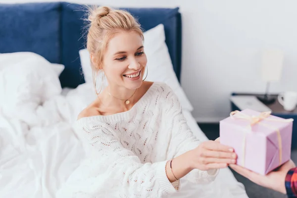 Hermosa mujer sonriente tomando caja de regalo del hombre en el dormitorio - foto de stock